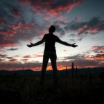 Silhouette of a man lifting his hands in praise, reflecting on God our Justifier who makes us righteous through faith in Jesus.