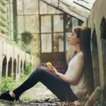 A woman sitting quietly in reflection inside a greenhouse, representing the Compassion Of God and finding comfort in His mercy during difficult seasons.