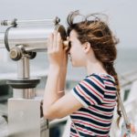 Girl looking through a telescope toward the sky reflecting on God who is Enthroned On High above the heavens.