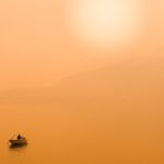 Peaceful scene of a boat on glowing water at sunrise, reflecting the beauty and majesty of our Glorious God