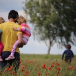 Father carrying his children through a field, reflecting the love and care of our Heavenly Father who watches over and guides us.