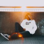 Woman sitting beneath bright sunlight wearing a “Kinda Bad” sweatshirt, illustrating that Jesus is the Son of God who sees our sin and calls us to repentance.