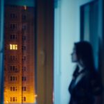 Person looking out a window at night, reflecting on feeling alone but remembering that God is for us and always present.