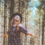 Woman joyfully standing in a sunlit forest, reflecting on the peace and strength found in the God of All Grace