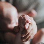 Baby holding an adult’s finger, reflecting on The Lord Our Maker who formed us from the womb.