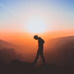 Person walking under a bright sunrise, reflecting on Jesus, the omniscient Son of God, who knows everything about us and still loves us.