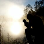 The silhouette of a man bowed in reverence to the Lord, set against the backdrop of a lake.
