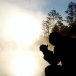 Person kneeling in prayer at sunrise, reflecting on God as I AM who is ever-present, active, and near to those who seek Him.