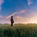 Man standing in a field under a vast sky, reflecting on Jehovah, the self-existent God who has no beginning.