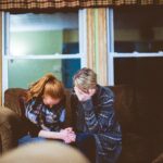 Two women sitting in prayer, trusting Jesus as Champion in difficult times