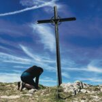 Person kneeling before a cross, worshiping Jesus as the King of the Jews.
