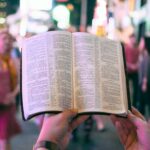Open Bible held up in a busy public setting, reflecting on how God is powerful to give wisdom and strength in troubling times.