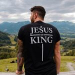 Man wearing a Jesus Is King shirt, reflecting on Jesus as the King of Saints who calls believers to honor Him.