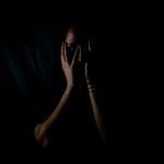 Woman sitting in darkness with her face in her hands, reflecting on God as our protector who gives peace in times of fear.
