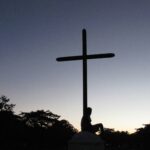 Person sitting beneath a cross, illustrating Jesus as a sacrifice to God on our behalf through His death on the cross.