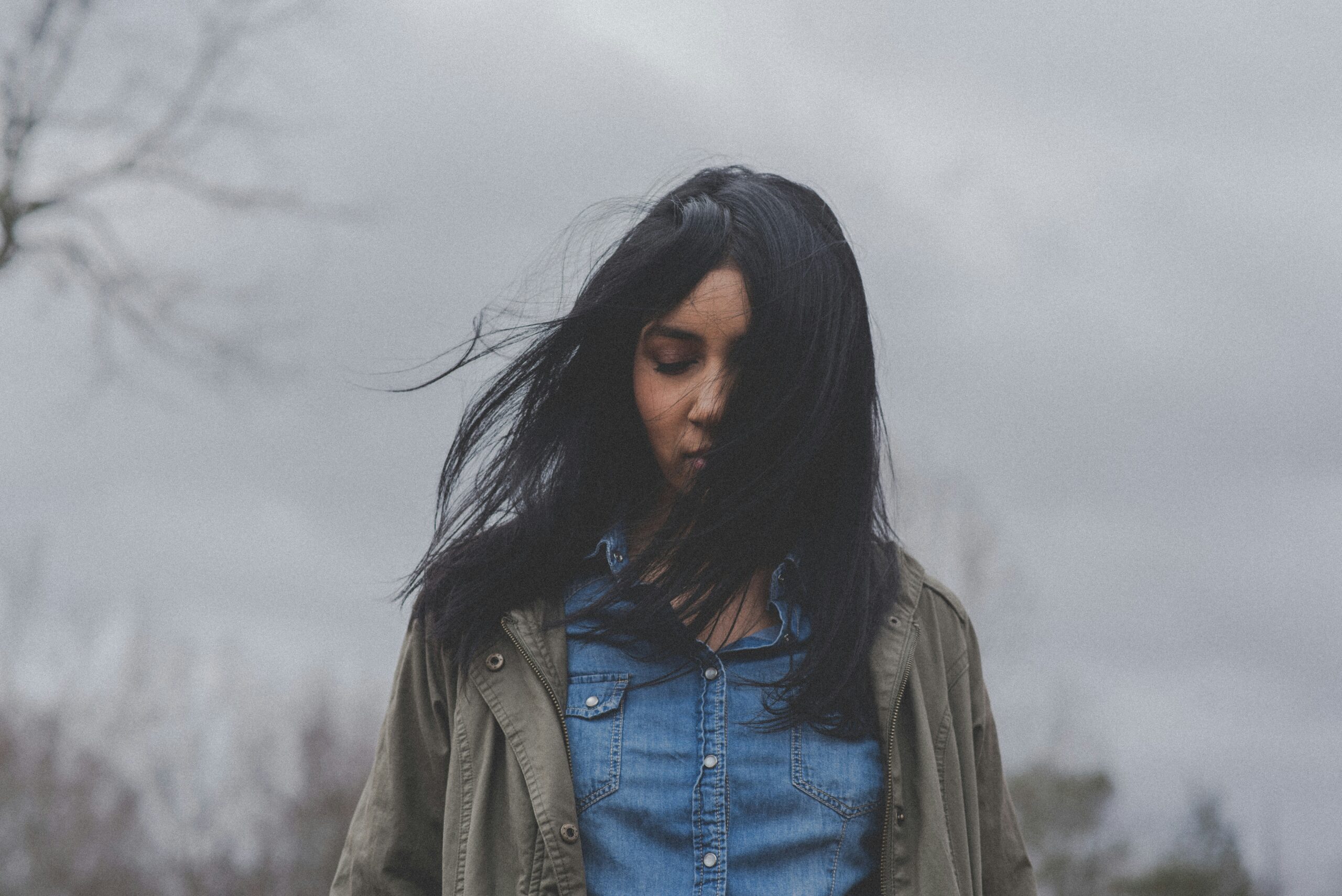 A woman walking outside. The woman and looks sad and the sky is overcast.