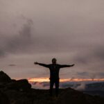 A man standing on a mountaintop, raising his hands in praise to the Almighty God.