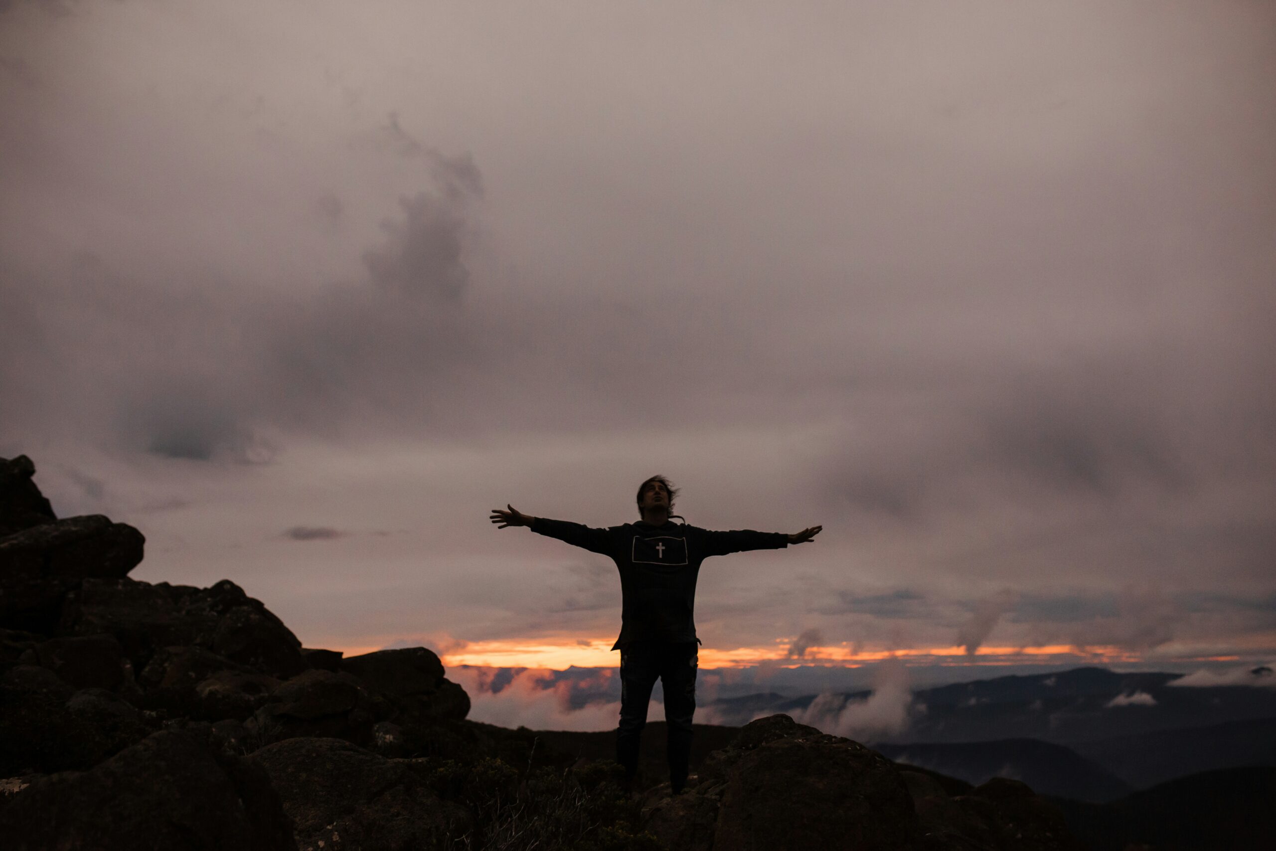 A man standing on a mountaintop, raising his hands in praise to the Almighty God.