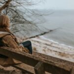 Woman sitting on a wooden bench overlooking the water, reflecting on how the Lord is Close To The Brokenhearted.