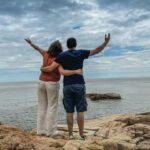 Couple standing together overlooking the water, symbolizing hope and eternal life through Jesus. the God of The Living, who gives life beyond death