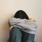 Woman sitting with her head down, reflecting on God as the Lifter Of Our Head who gives hope, peace, and grace.