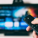 Hand holding a TV remote in front of a television, illustrating the need to stand against pornography and harmful media content.